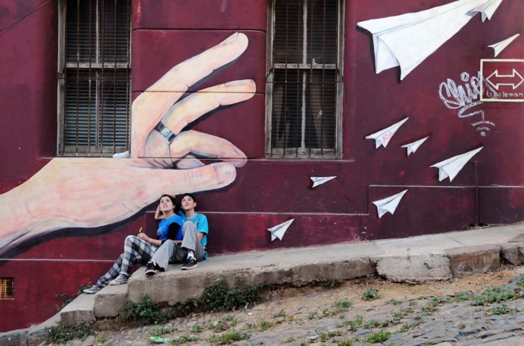 Valparaiso, Chile: children sitting in front of a mural looking at an airplane flying overhead
